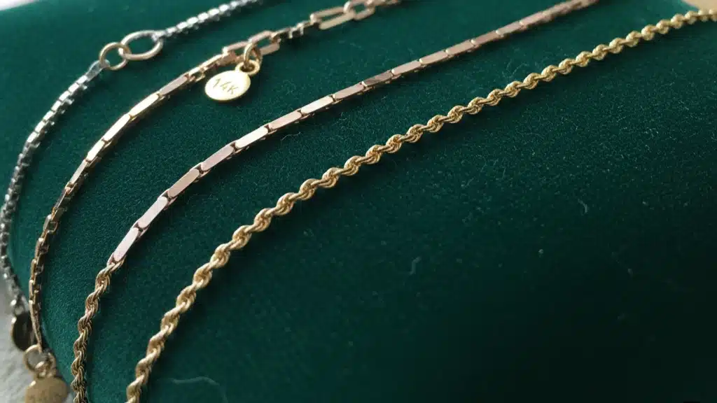 Collection of delicate gold chains in various styles including rope chain, link chain, and flat chain designs displayed on green velvet - quality foundation pieces and jewelry gift ideas perfect for graduation gifts, serving as versatile base chains for any jewelry collection that transition from casual to formal occasions